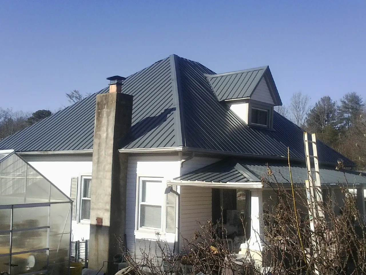 Dark blue standing seam metal roof on a white farmhouse with dormer — Slate & Tile Roof Repair by Roofing Brothers in Glade Hill