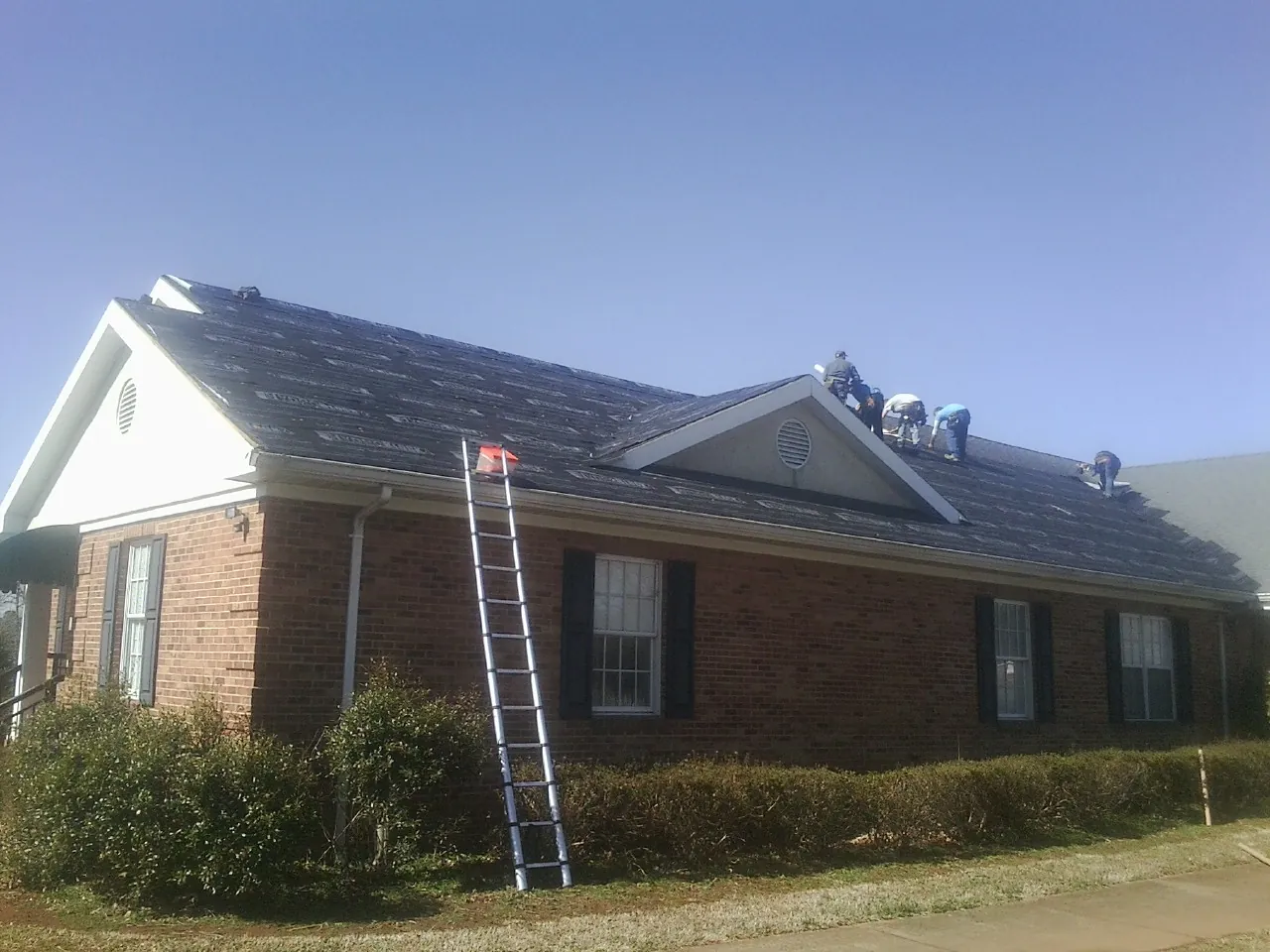 Crew tearing shingles off a brick ranch roof with a ladder set — Emergency Roof Repair work by our crew in Glade Hill