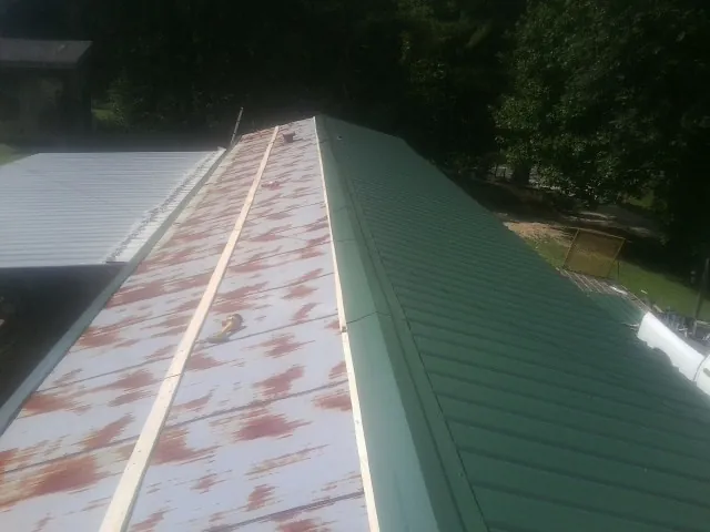 Old rusted panels beside newly installed green metal roofing — Wind Damage Roof Repair by Roofing Brothers in Glade Hill