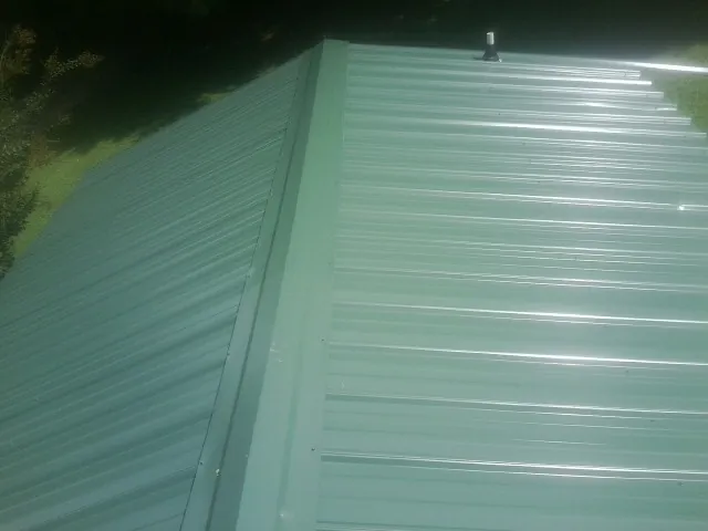 New green metal panels meeting at the ridge of a roof — Flat Roof Repair work by our crew in Glade Hill