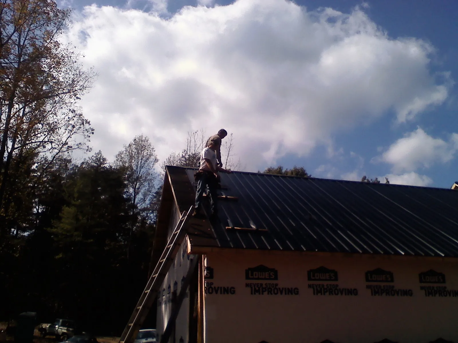 Roofer fastening dark metal panels high against a cloudy sky, from a Roof Inspection job in Glade Hill