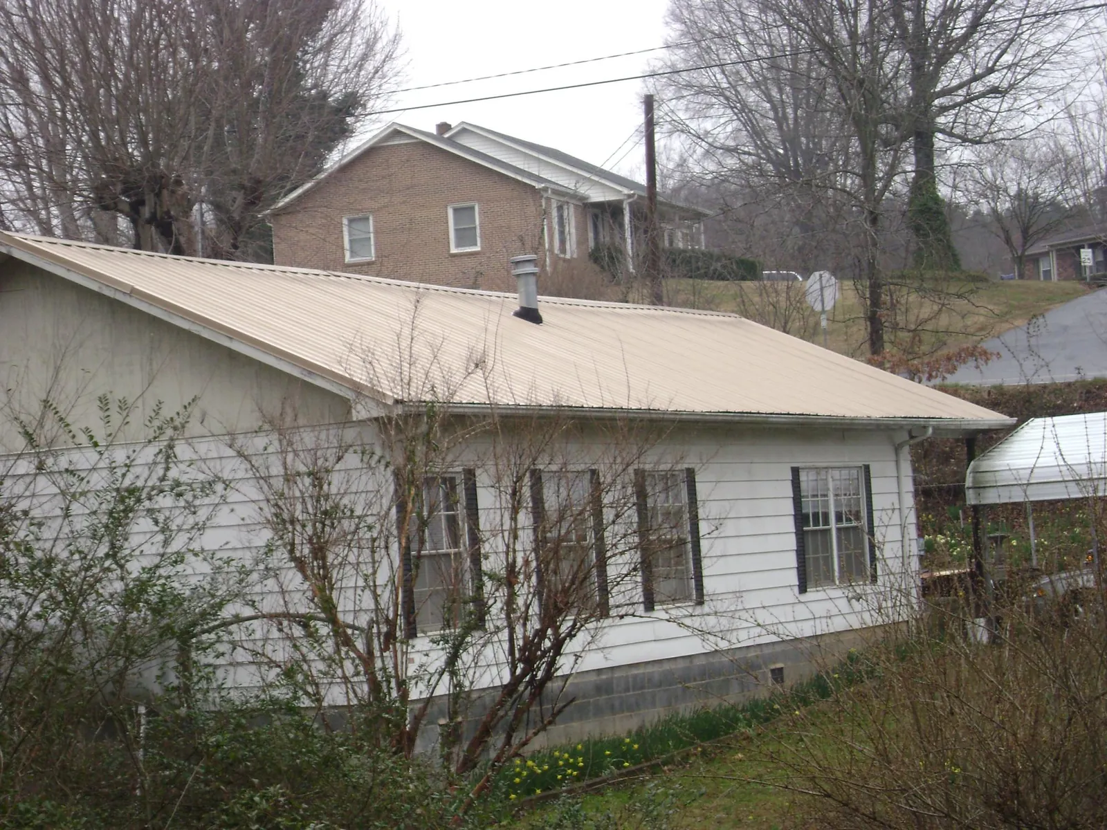 Tan metal roof on a white sided house set into a hillside — Commercial Roofing by Roofing Brothers in Glade Hill