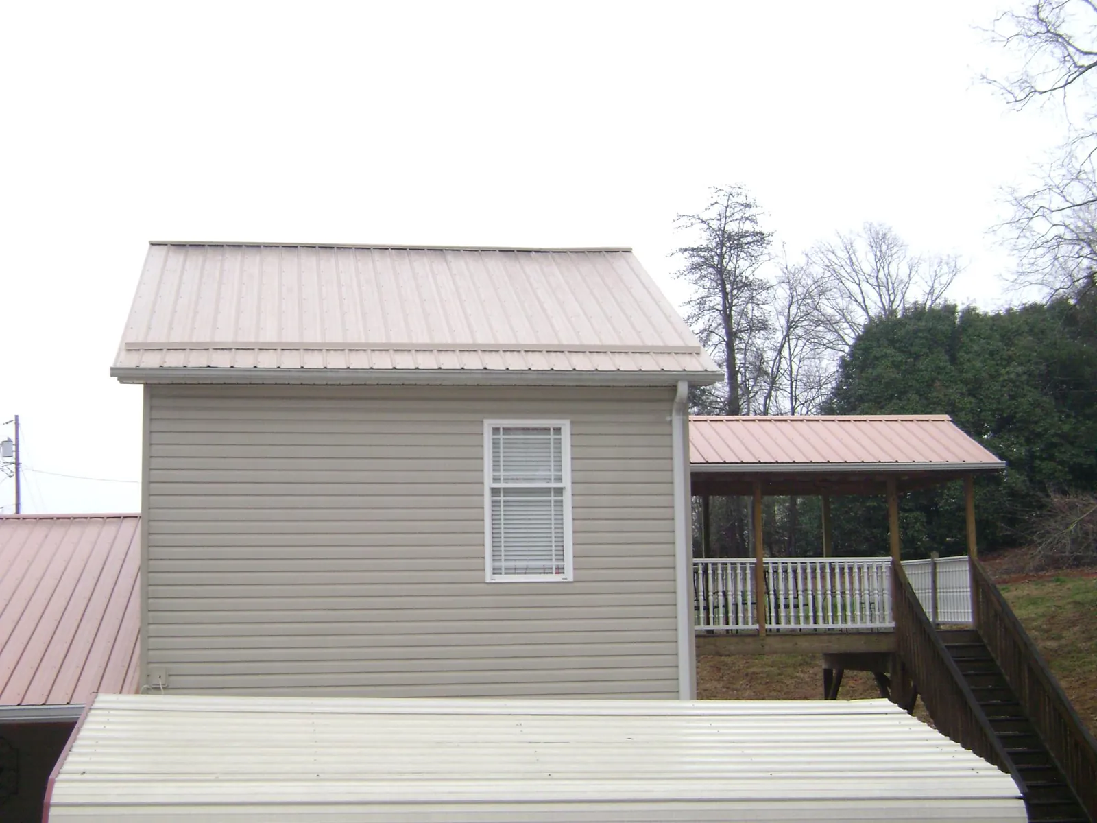 Tan metal roofs on a two story addition and attached porch, from a Roof Replacement job in Glade Hill